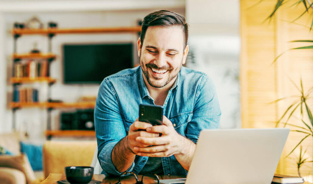 Man sat at a laptop accessing Vitality Hub on a mobile phone