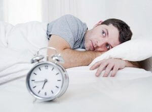 Man awake in bed next to alarm clock